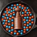 A skillet filled with rich skillet brownies batter, decorated with orange and blue candy-coated chocolates, featuring a large chocolate trophy in the center.