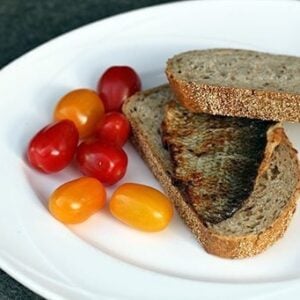 whitefish fillets, slices of bread and fresh small tomatoes in a white plate