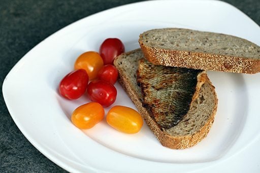 whitefish fillets, slices of bread and fresh small tomatoes in a white plate