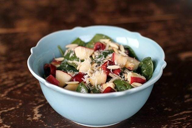 Close up of Apples N' Cherries Spinach Salad in a blue Pyrex bowl