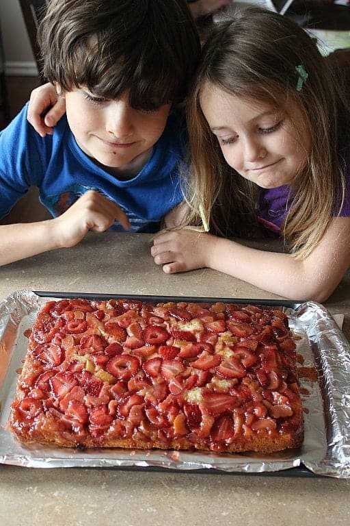 photo of kids looking at Strawberry rhubarb upside down cake on a baking tray