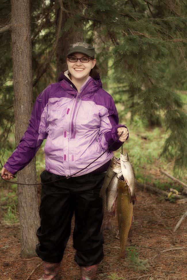 woman in violet jacket holding a string with all caught brook trout