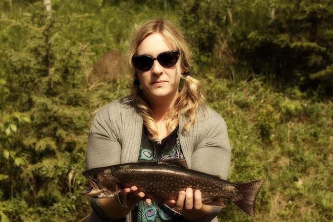 woman in sun glasses holding a brook trout fish