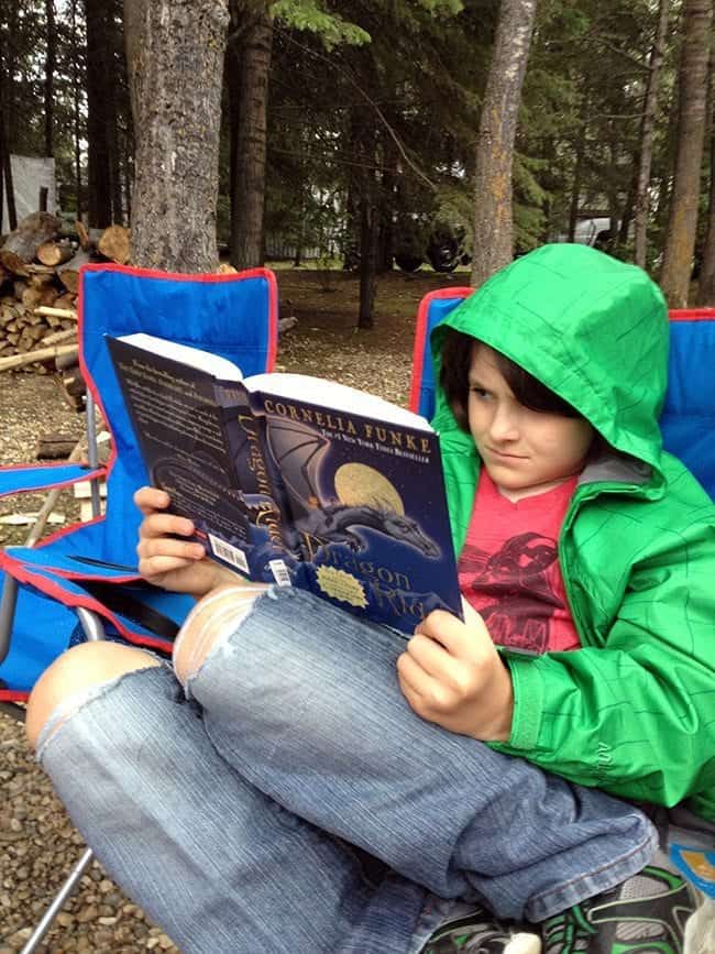 young boy reading a book while sitting in a camping chair