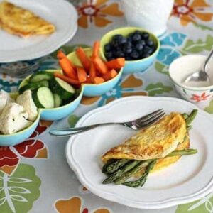 plates with asparagus and cheese omelettes, serving dishes with vegetables and blueberries on the table