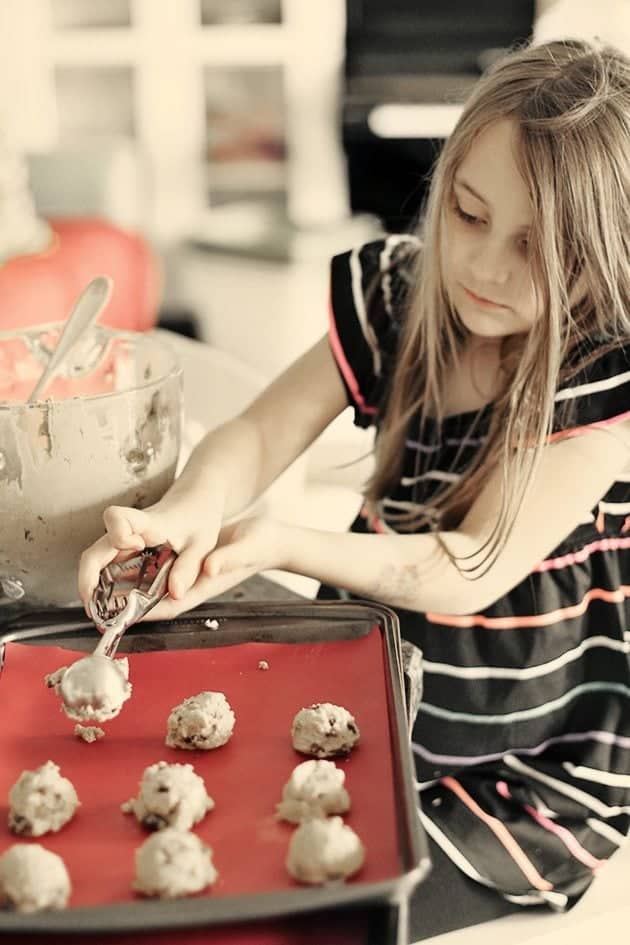 little girl uses a cookie scoop to shape the Raisin Molasses Gems 