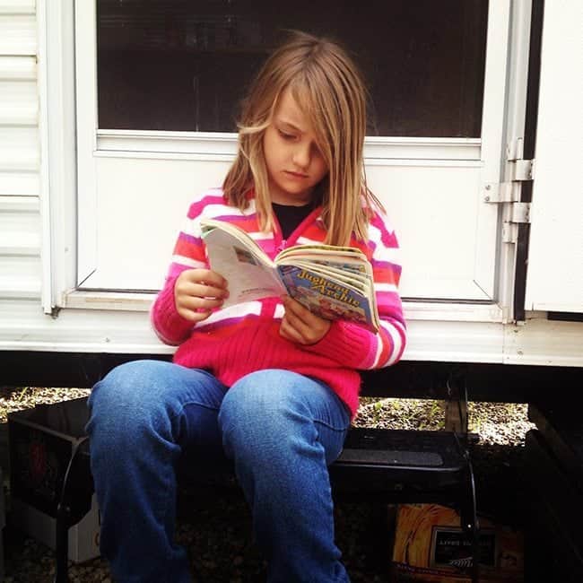 young girl reading a book while sitting near the white door