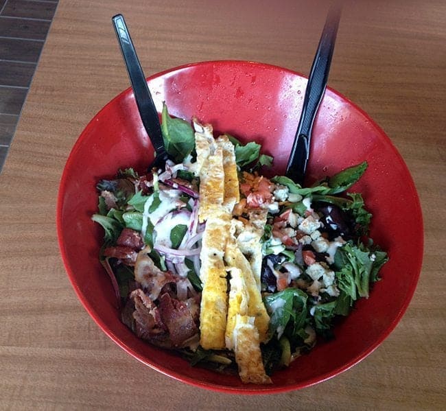 Cobb salad with fried egg on top and applewood smoked bacon, all in a red bowl