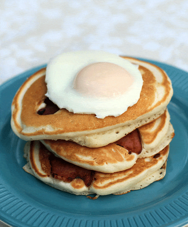 stack of three pieces bacon pancakes with fried egg on top in a plate