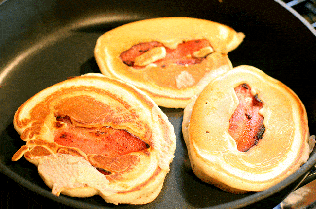 piece of bacon in the middle of the batter of each uncooked side of pancakes in skillet