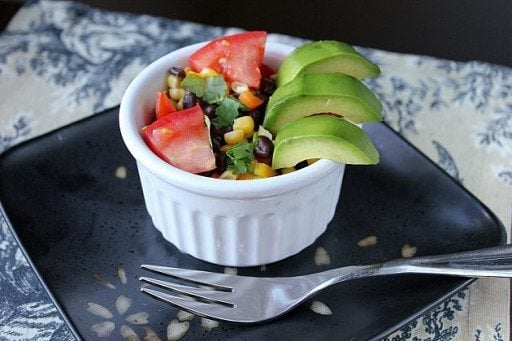 Avocado, black bean and corn salad in a ramekins on black plate with fork