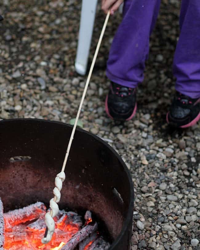 cooking the wrapped biscuit dough over a campfire