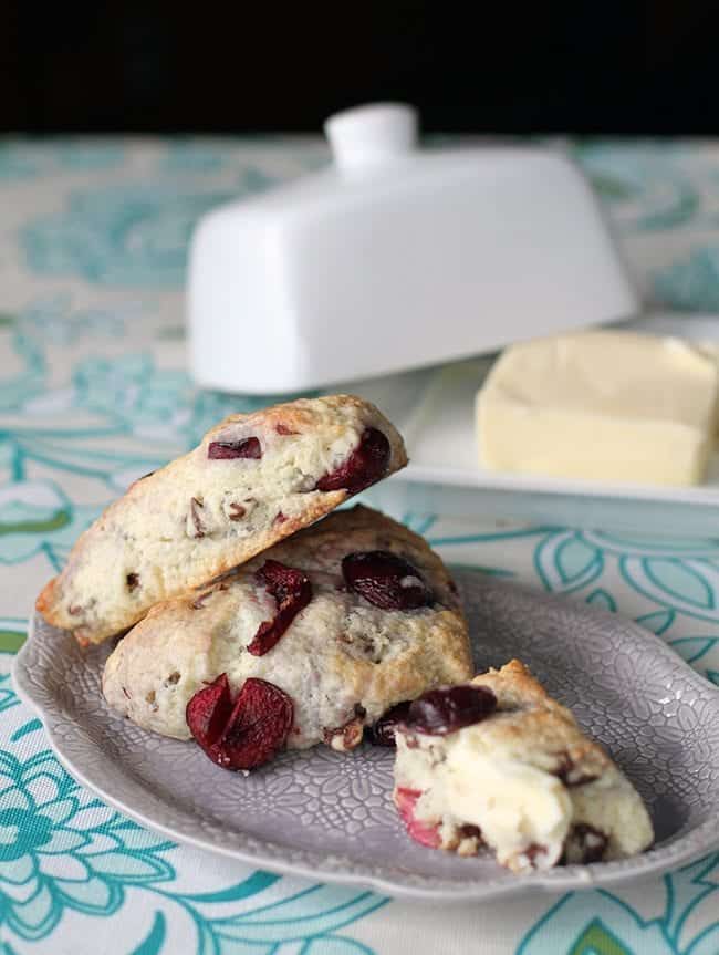 close up of three chocolate cherry scones in a plate, whole butter in a plate on background