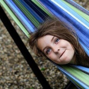 little girl rolled herself up in the blue and green colored hammock