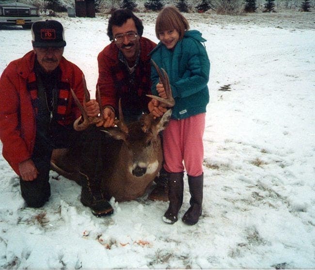 two men and a child holding at the deer's antlers
