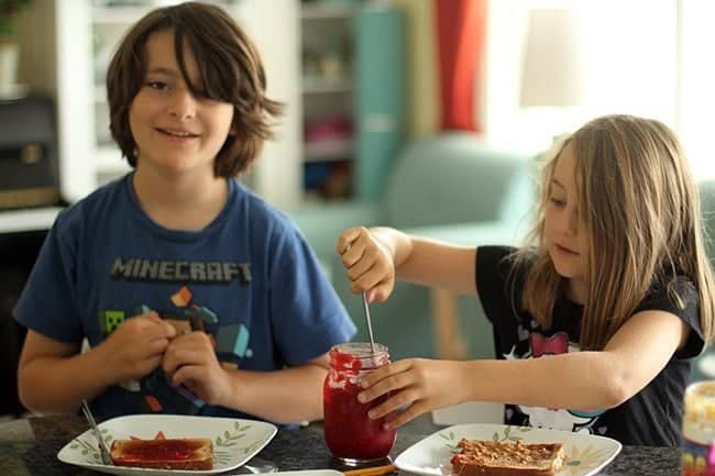 two kids spreading Homemade Raspberry Jam in a slice of bread