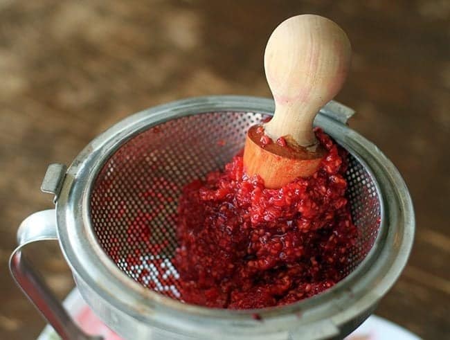 crushing the fresh raspberries in chinois using wooden pestle