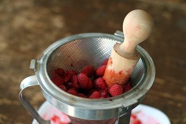 fresh raspberries in chinois with the wooden pestle