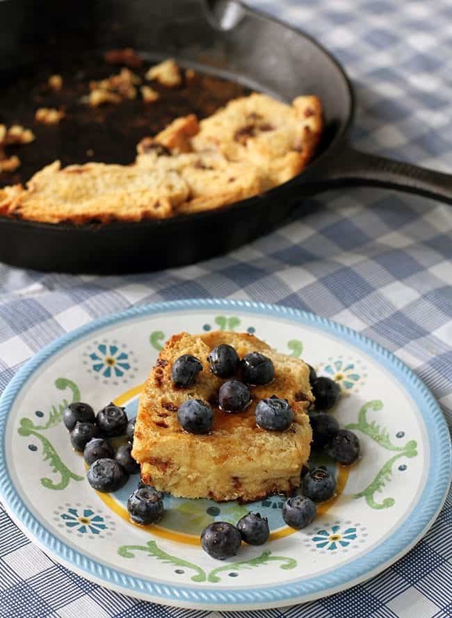 close up of Baked French Toast with maple syrup and fresh blueberries in small dessert plate, skillet with slices of pie on background