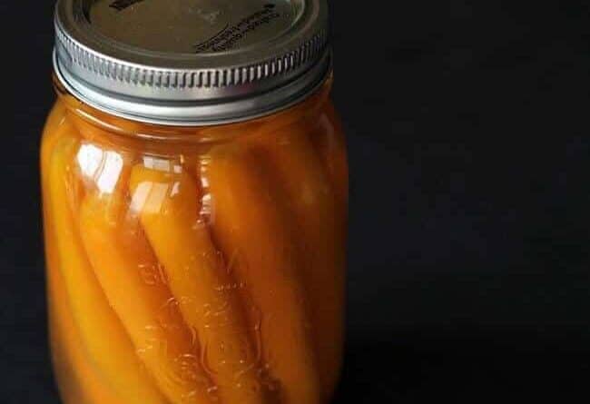 close up of sweet Pickled Carrots in a canning jar with pickling liquid in a dark background
