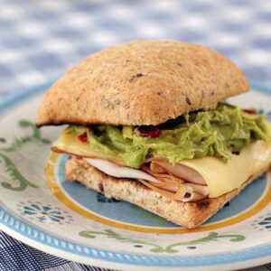 toasted buns with turkey at the bottom, top with Swiss cheese, guacamole and mastard