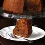 dense and chock full pumpkin Bundt Cake in a cake holder and a slice in white dessert plate with fork