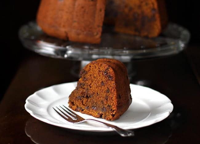 dense and chock full pumpkin Bundt Cake in a cake holder and a slice in white dessert plate with fork