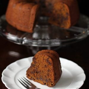 dense and chock full pumpkin Bundt Cake in a cake holder and a slice in white dessert plate with fork