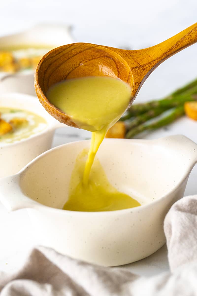 wooden ladle spooning asparagus soup into a white bowl