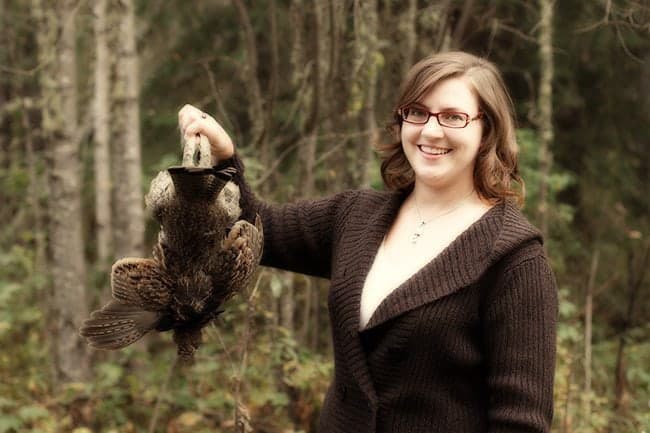 woman with glasses holding the fallen ruffed grouse upside down