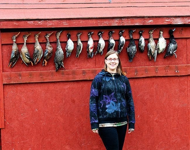 close up of woman standing in front of requisite duck wall where fallen ducks are hanging