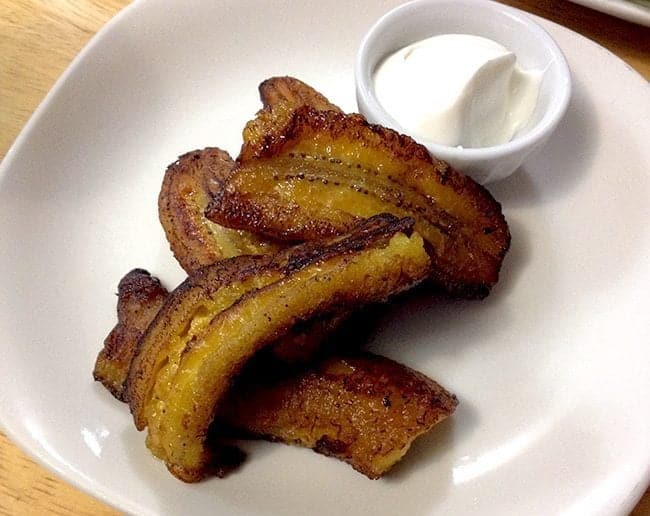 Fried Plantains in a white plate with a cup of sour cream beside it