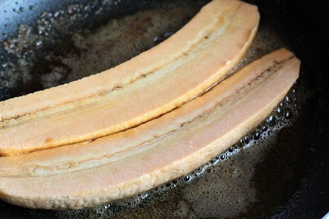 Plantains peeled and sliced in the half length-wise in a skillet with melted butter