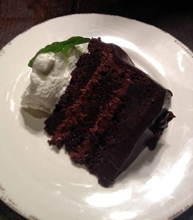 a slice of chocolate cake with white icing on top in a white plate