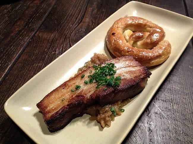 crispy pork belly with fennel confit and a homemade salted pretzel in a white rectangular plate
