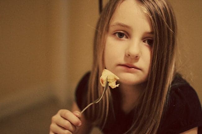 close up of young girl holding a fork with slice of an apple