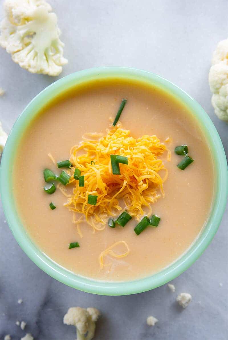close up Cheesy Cream of Cauliflower Soup in a soup bowl with grated cheddar cheese and chopped green onion