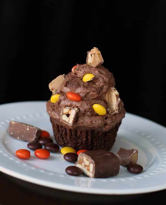 Buttercream Icing with chopped up candy bars on top of chocolate cupcake in a plate