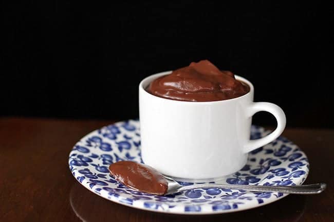 Homemade Chocolate Pudding in a white mug on a blue designed small plate with spoon on side