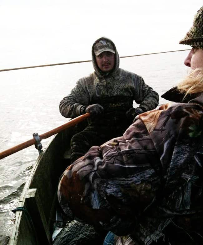 two men wearing their duck hunting gear, rowing a boat