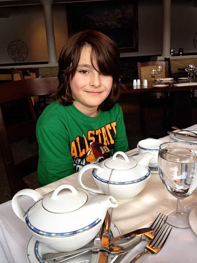 kid in green shirt sitting beside the table while wailing for the tea