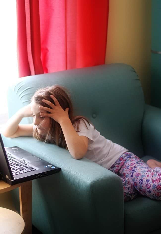 young girl in the couch holding her head while watching something in the laptop