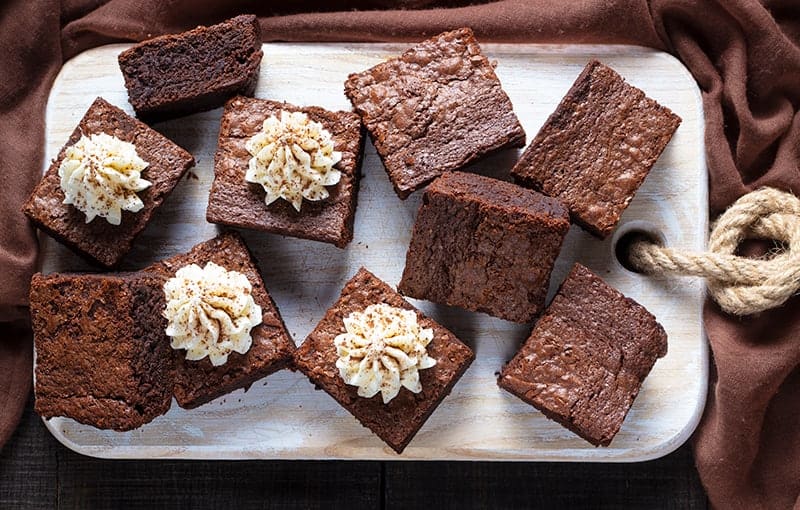 Mint Brownies with Buttercream Icing on wooden cutting board with brown tablecloth underneath