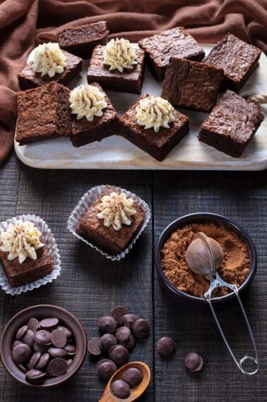 Mint Brownies with Buttercream Icing on wooden cutting board with brown tablecloth underneath and its ingredients on side