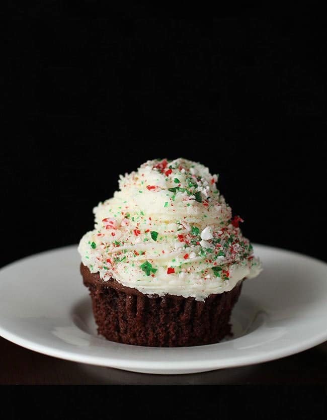 Peppermint Buttercream Frosting with crushed candy cane on top of chocolate cupcake in a white plate