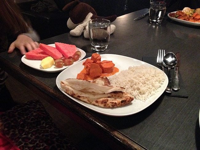 a plate with rice and butter chicken with another plate of sliced fruits