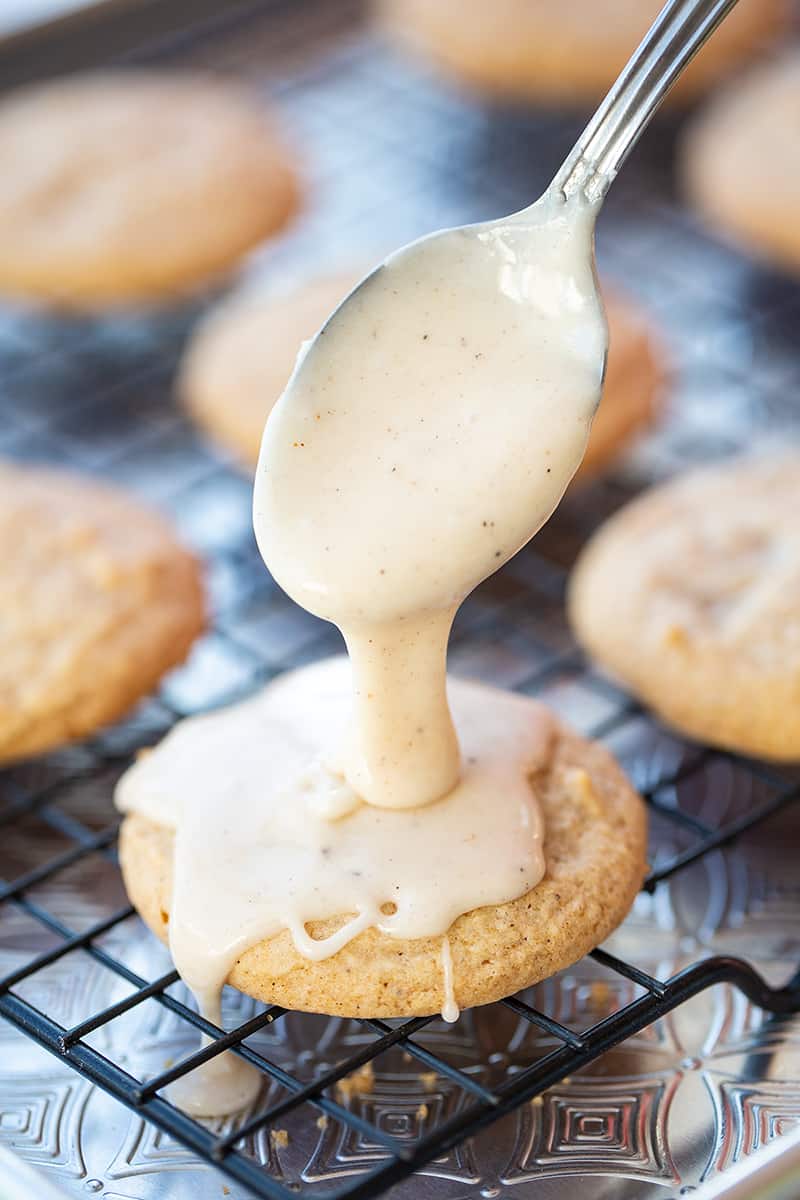 a spoon of eggnog glaze added to the cookies on a cooling rack