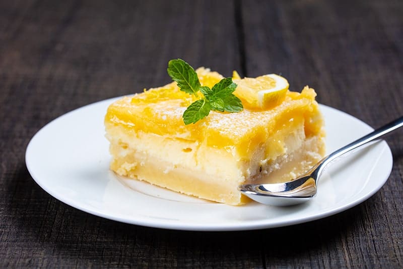 white plate with a spoon and Lemon Cheesecake Bar garnish with lemon balm leaves