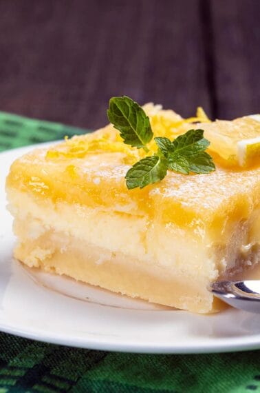 close up white plate with Lemon Cheesecake Bar garnish with lemon balm leaves