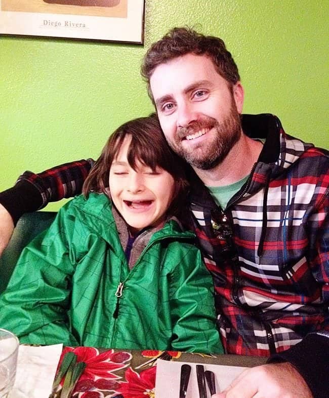 son wearing green and dad wearing checkered red blue sitting inside Red Iguana restaurant